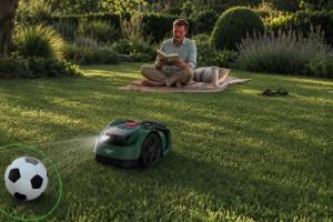 A robot lawn mower at work with a man sitting on the lawn nearby
